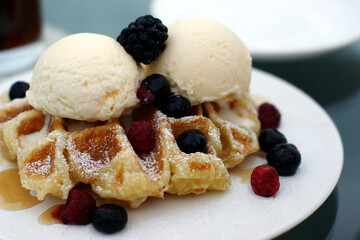 Dessert with ice cream, fruits and syrup on top of waffles.