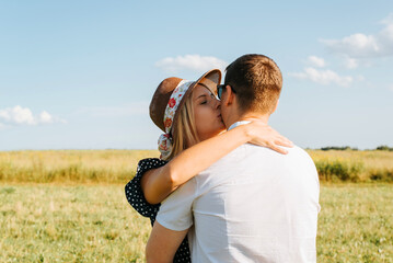 Pretty young woman in astraw hat hugs and kisses man outdoors on sunny day. Caucasian heterosexual love couple flirting in nature, romantic relationship