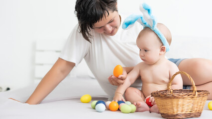 Obraz na płótnie Canvas Mother and child with colorful eggs. Mom and baby with bunny ears. Parent and kid play indoors in spring. Family celebrating Easter