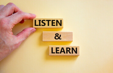 Listen and learn symbol. Concept words Listen and learn on wooden blocks. Beautiful white table white background. Businessman hand. Copy space. Business, educational and listen and learn concept.