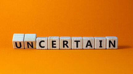 Certain or uncertain symbol. Turned wooden cubes and changed the concept word uncertain to certain. Beautiful orange table, orange background, copy space. Business, certain or uncertain concept.