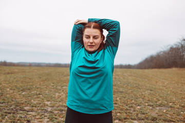 Chubby caucasian woman doing morning stretching exercises in natural autumn park.