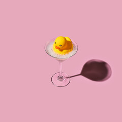 Yellow toy rubber duck floating in a martini glass with bubble foam. Creative abstract bathing concept