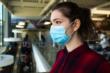 Beautiful pretty worried caucasian young woman wearing protective surgical face mask, standing in a...