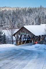 Snow covered Covered Bridge in New England with evergreens in the background.