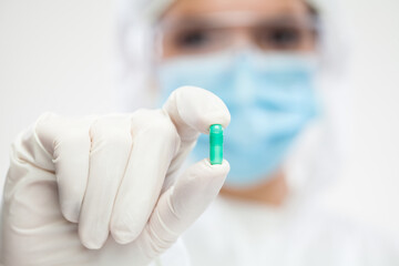 Female pharmacist wearing PPE personal protective equipment holding green pill