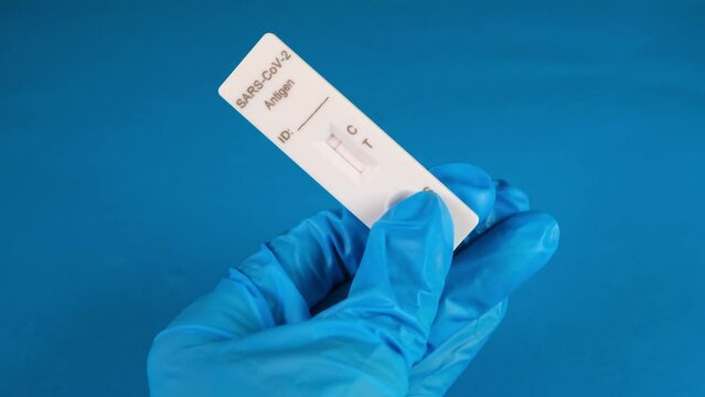 hand in a protective medical glove holds a Negative SARS-CoV-2 Rapid Antigen Test on a blue background