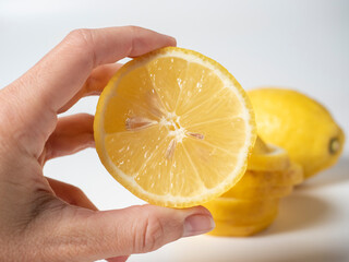 Close-up of a hand holding half a lemon. Sliced lemon in the background. white background. Sour healthy fruit