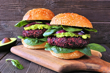 Healthy plant based beet burgers with avocado and spinach. Side view on a wooden board against a rustic dark wood background.