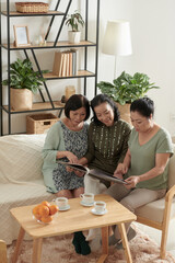 Female senior friends looking at old photos in photo album when gathering at home for small party