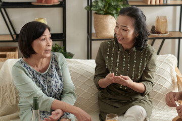 Serious senior woman discussing problems with best friends when they are drinking wine at home