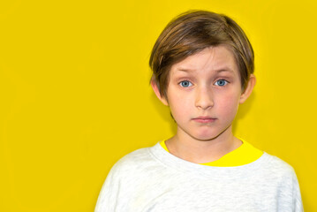 handsome schoolboy sad or serious on yellow background. portrait of a boy, a child, a kid in gray clothes