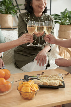 Cropped image of senior women clinking glasses of champagne oved table with tasty food at home