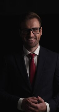young handsome businessman crossing his arms, smiling, wearing eyeglasses and nodding on black background