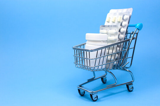 Shopping medicine concept. Medical pills, tablets, capsules and white drug bottle in shopping cart or shop trolley on blue background. health care, health insurance and pharmaceutical company.