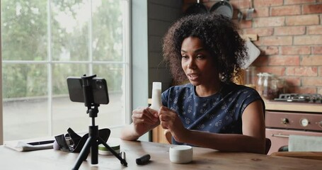 African female video blogger influencer shoot tutorial on smartphone advertise body care cosmetic line. Young woman beauty expert film promo content make product review introduce new brand to audience
