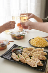Plate with delicious homemade jiaozi and soy sauce on dinner table, guests toasting with wine glasses in background