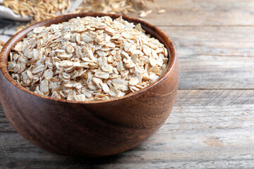 Bowl with raw oatmeal on wooden table. Space for text