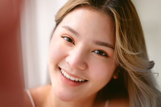 Closeup portrait of inspired young Asian lady smiling friendly taking selfie photo in bedroomin the morning. Concept woman lifestyle,  Beauty and healthy Woman. Express positive enthusiastic emotion