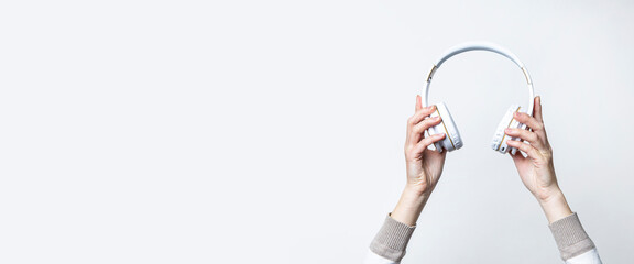 Female hands holding large white headphones on a light background. Banner.