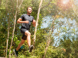Handsome Caucasian male runner running in the natural park. Dynamic running uphill on trail....