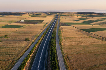 Empty highway stretches to horizon through plain with fields and olive plantations, Halkidiki Greece