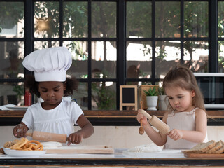 Little Dark skinned and Caucasian girls playing with rollers for baking dough. Diversity and Education concept.