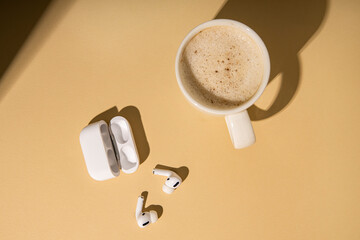 Coffee, wireless headphones on a beige background. Flat lay, top view.