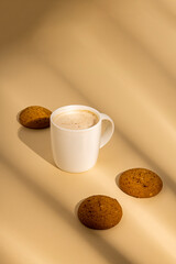 Cappuccino in a white cup, oatmeal cookies on a beige background.