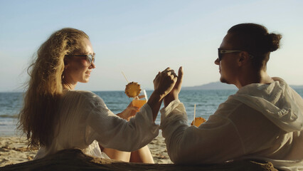 Loving couple in white dress, sunglasses, relax and drinking cocktail Pina Colada. Man kissing hand...