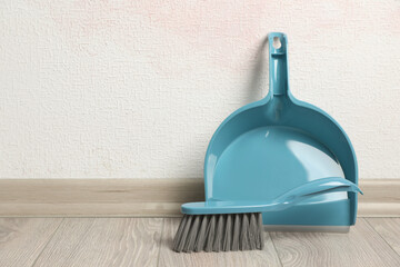 Plastic whisk broom with dustpan near light wall indoors. Space for text