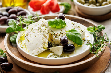 Feta cheese with the addition of olive oil, olives and herbs on a ceramic plate on a rustic wooden table. Traditional Greek products - 486939893