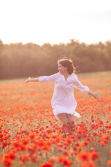 Naklejka na ściany i meble Beautiful girl in a white dress on a poppy field