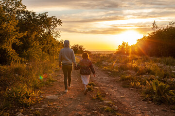 Fototapeta na wymiar Mom and daughter are walking along the road at sunset, around beautiful landscapes from the mountains