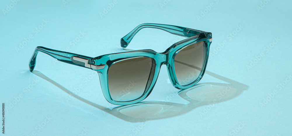 Wall mural sunglasses on pastel blue background in sunlight. modern stylish sunglasses for beautiful holiday va