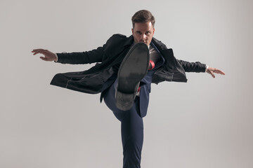 elegant young guy in suit with long coat holding leg up and kicking