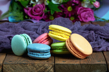 French macaroni on the background of a beautiful bouquet of flowers lie on a wooden background. Close-up.