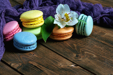 French macaroons and one flower surrounded by blue fabric lie on a wooden background. copy space. ..