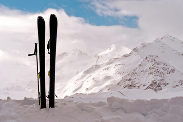 Vertically standing skis in the snow against the backdrop of snow-capped mountains.