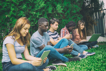 Fototapeta na wymiar High school multi ethnic students relaxing using electronic gadgets outdoor.