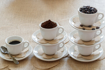 caffee cups with various stages of caffee, coffee beans, grinded coffe and coffee in a cup