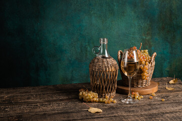 A glass of homemade white wine with grapes and a bottle on a rustic wooden table