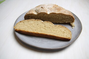 Fresh just baked rye  bread loaf and slice on gray plate on white background