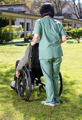 Obraz premium Caucasian senior on the wheelchair helped by nurse outdoor. Retired elderly people living their life at its best.