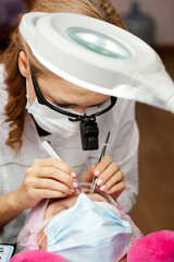 A girl makes the procedure for extending eyelashes during a pandemic, a master with tools in her hands