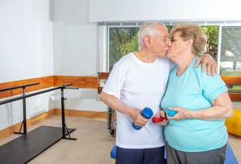 Happy couple of seniors smiling training at the gym and kissing each other. Retired elderly people living their life at its best.
