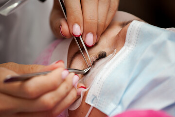 A girl makes the procedure for extending eyelashes during a pandemic, a master with tools in her hands