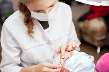 A girl makes the procedure for extending eyelashes during a pandemic, a master with tools in her hands