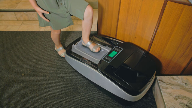 Automatic Thermal Shrinkable Shoe Cover Laminating Machine. Close up dispenser in hospital hall. Machine automatically applies shoe covers to the patient shoes, in operation, sterility, hygiene.