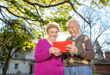 Caucasian seniors smiling outdoor using tablet. Retired elderly people living their life at its...